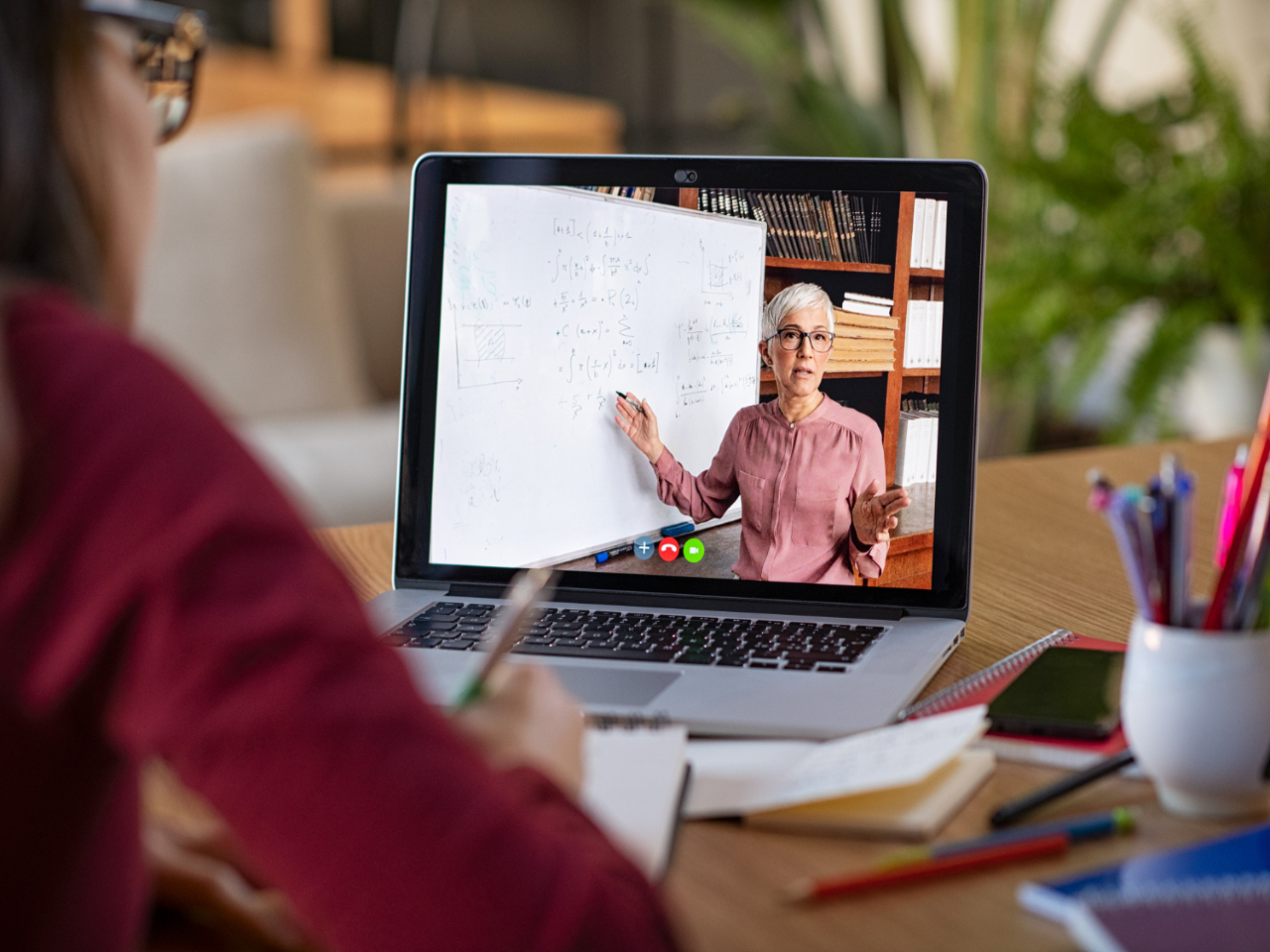 Mulher fazendo uma aula de pós-graduação ao vivo pelo notebook. Na tela, a professora explica alguns cálculos presentes no quadro branco.