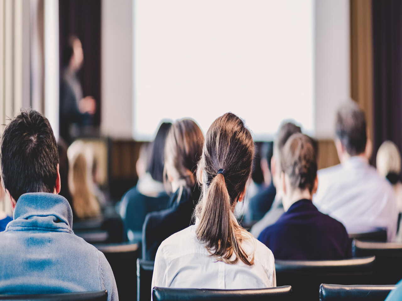 Aulas magnas de outubro: visão traseira de pessoas em um auditório, acompanhando uma palestra.