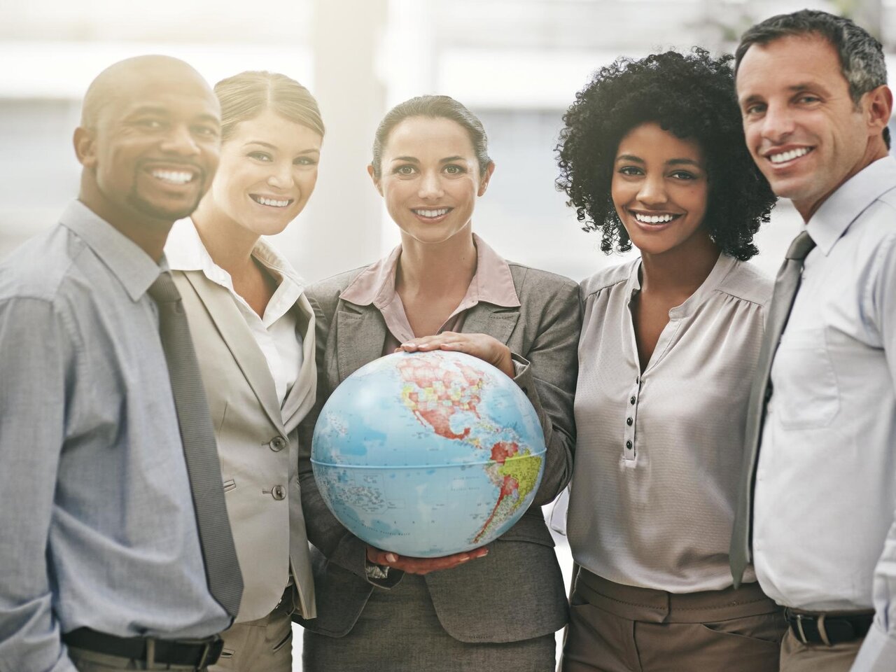 Cinco profissionais sorrindo para a foto enquanto um deles segura uma globo terrestre, representando o desejo de construir uma carreira internacional.