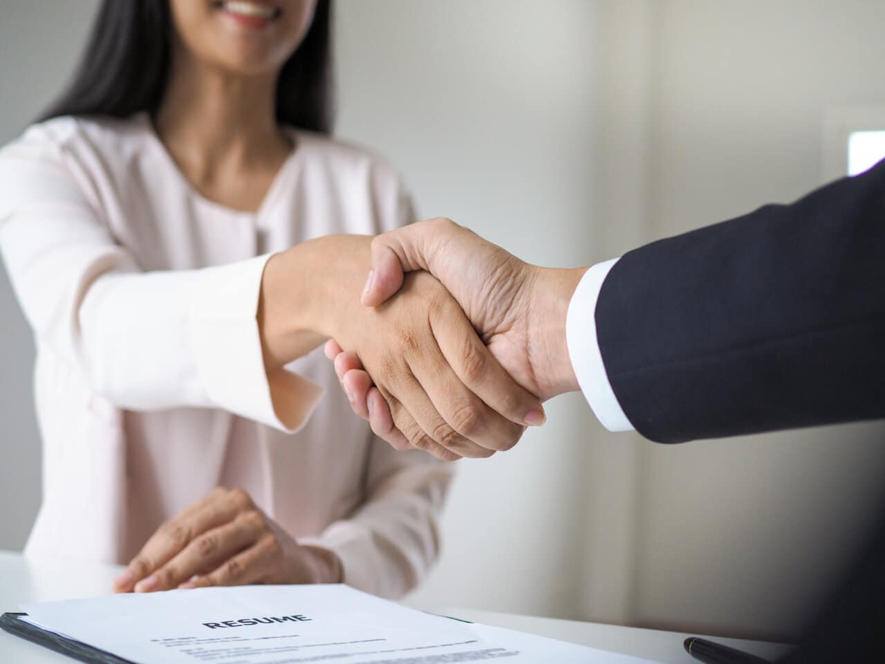 Mulher em busca de uma recolocação profissional apertando a mão de um recrutador após ser contratada para o novo emprego.