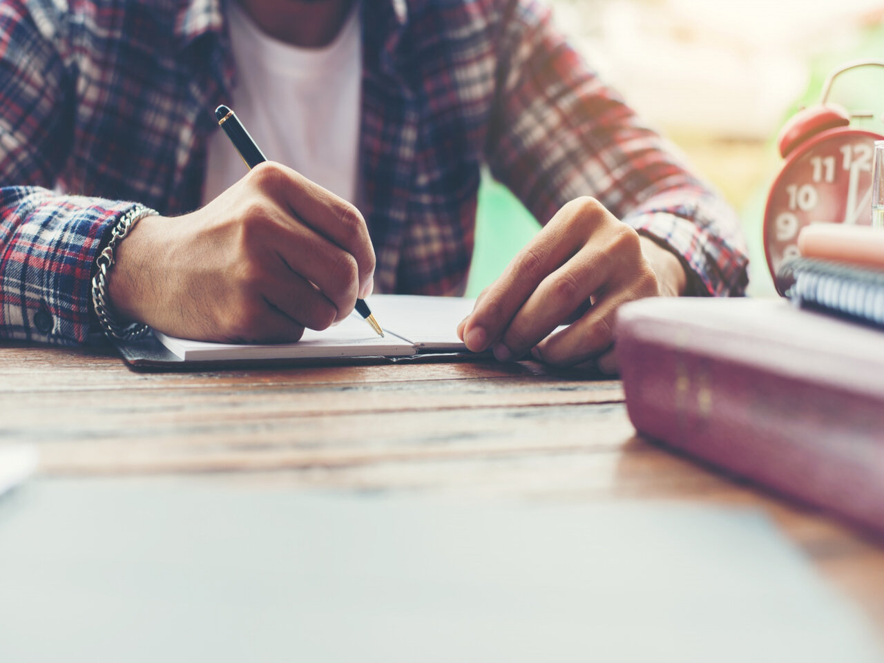 Tipos de discurso: estudante utilizando uma caneta para escrever um texto em um caderno.