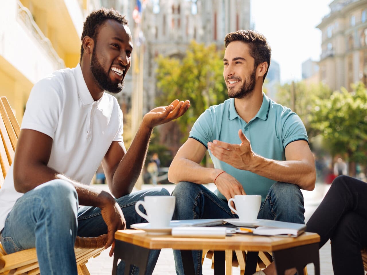 Linguagem culta e coloquial: dois homens sentados na área externa de uma cafeteria, tomando um café enquanto conversam de maneira informal.