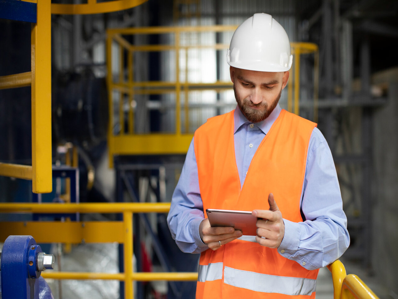 Engenheiro de produção segurando um tablet, usando um capacete branco em uma fábrica.