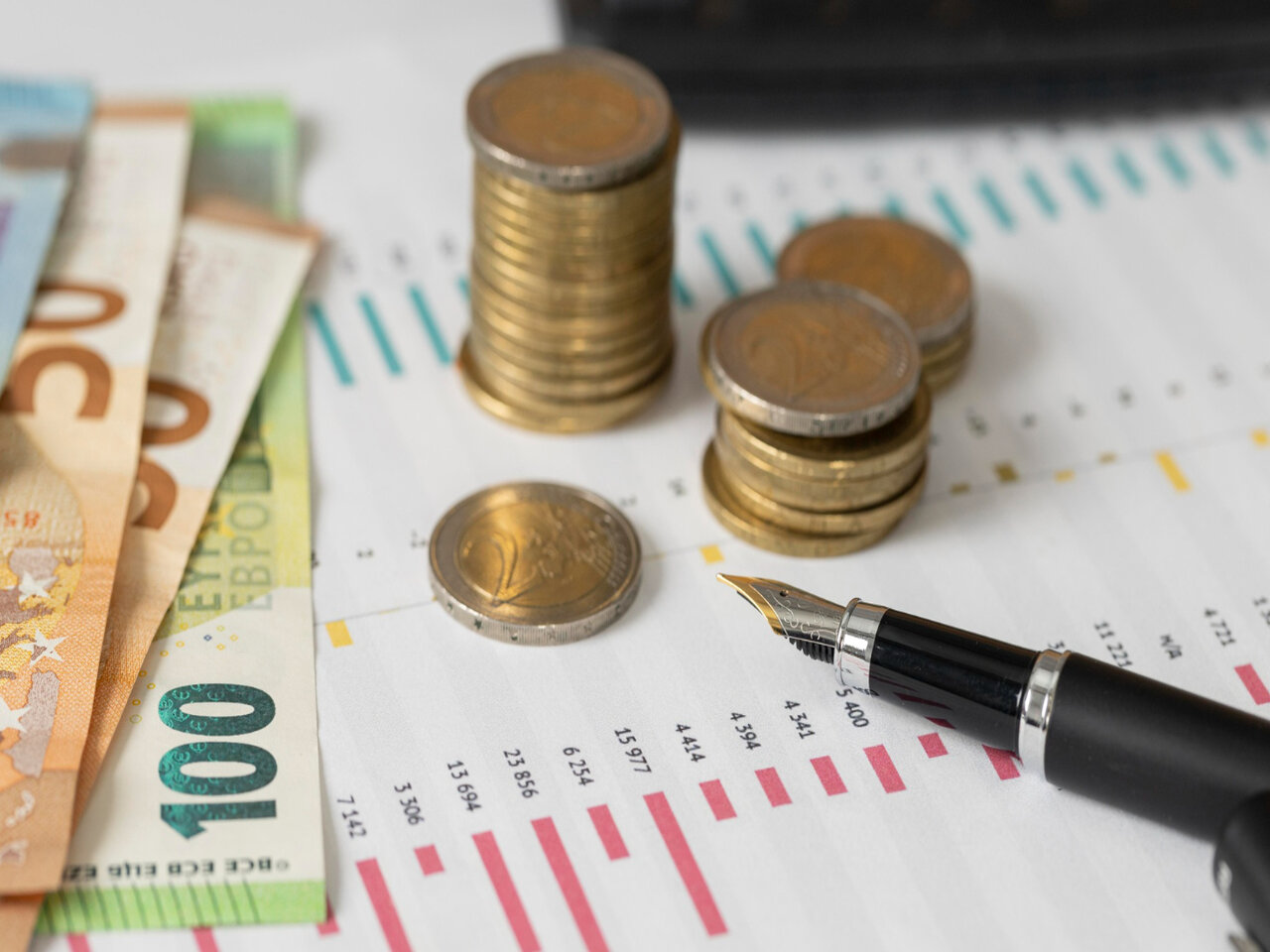 Faculdade de Ciências Econômicas: algumas moedas, uma caneta e notas de dinheiro em cima em cima de uma folha de papel com um relatório financeiro impresso.