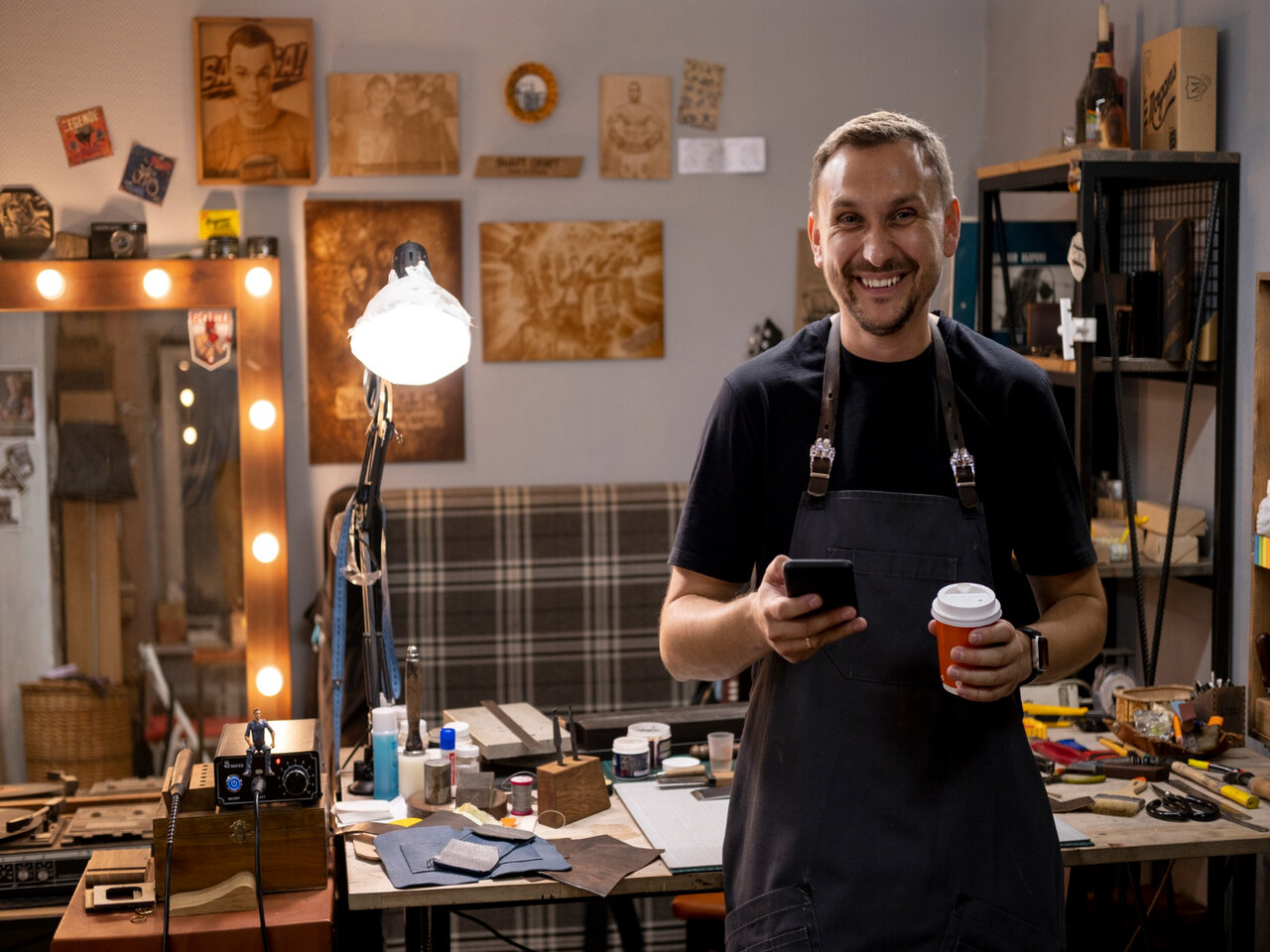 Microempreendedor em sua oficina, segurando um copo de café enquanto utiliza o celular para emitir a nota fiscal MEI
