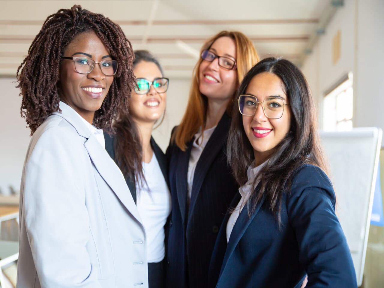 Empreendedorismo feminino: quatro jovens mulheres empreendedoras em um escritório, sorrindo para a foto.