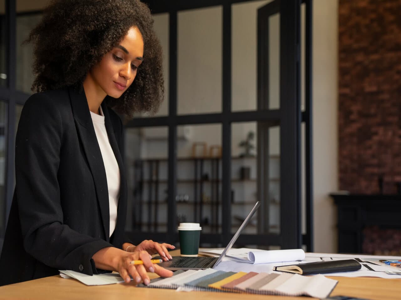O que é administração: administradora de uma empresa em seu escritório analisando alguns relatórios. Na mesa à sua frente, um notebook aberto e diversos documentos.