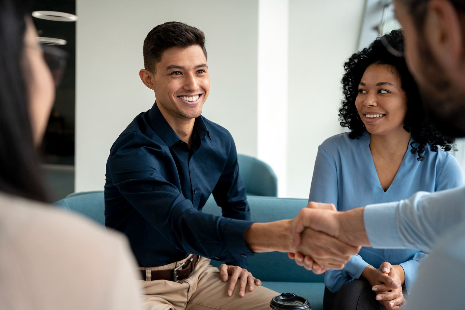 Experiência profissional: jovem rapaz sorridente em uma sala de reunião, apertando a mão de seu empregador após ser contratado. Ao seu lado, uma mulher sorri, em sinal de comemoração.