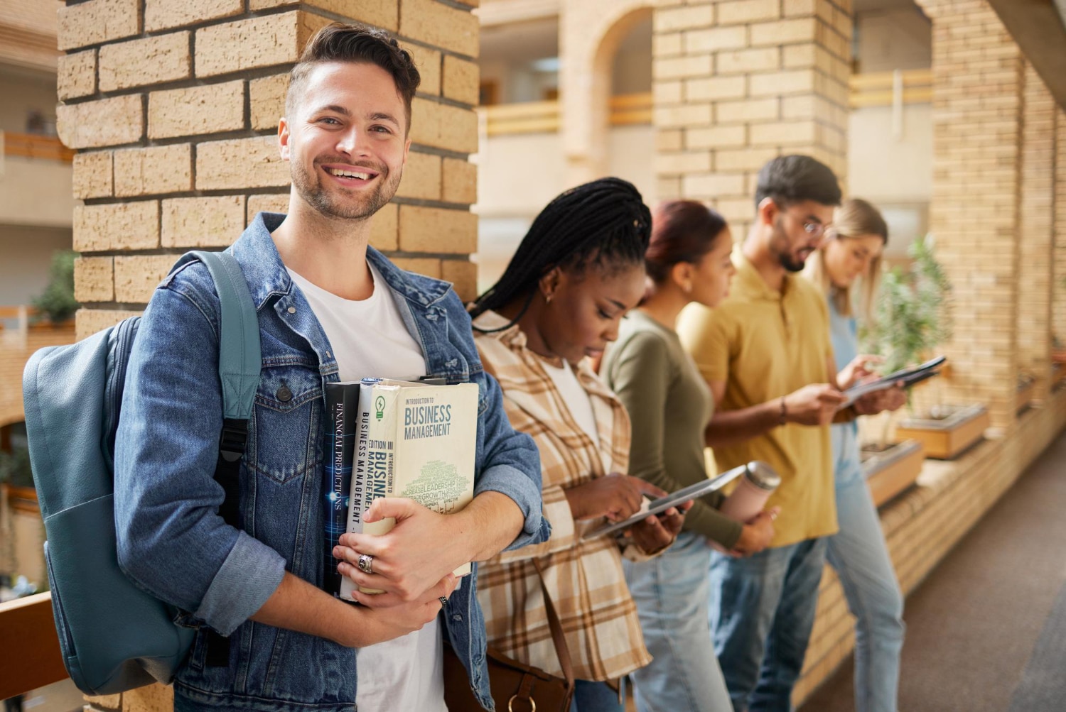 Grade curricular: cinco alunos no corredor de uma faculdade, utilizando mochila e segurando livros durante o intervalo das aulas.