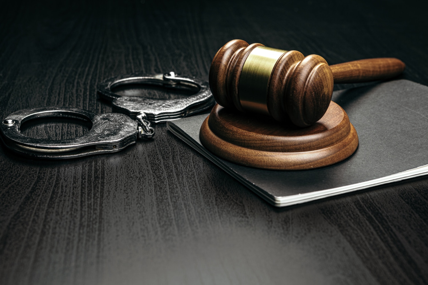 Imagem de uma mesa com um malhete, um livro e um par de algemas em cima, representando o direito penal e processo penal.