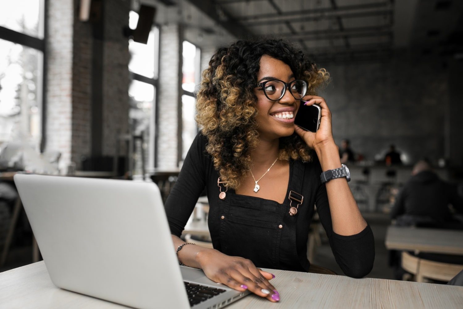 Teorias da administração: administradora em um escritório, sorridente enquanto fala no celular. Na mesa à sua frente, um notebook aberto utilizado para trabalhar.