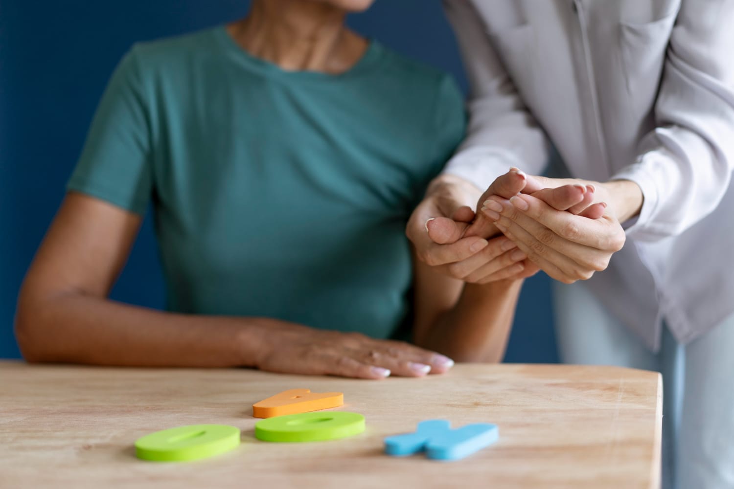 Tipos de terapia ocupacional: terapeuta ocupacional durante uma sessão auxiliando uma paciente idosa a reabilitar movimentos das mãos, mexendo em seus dedos.