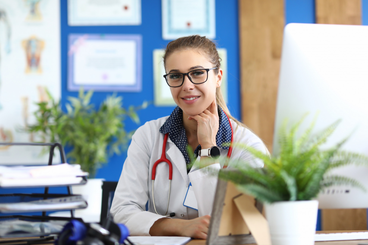 Faculdade de Gestão Hospitalar: Administradora de um hospital em seu escritório, com um estetoscópio no pescoço, sorrindo para a câmera.