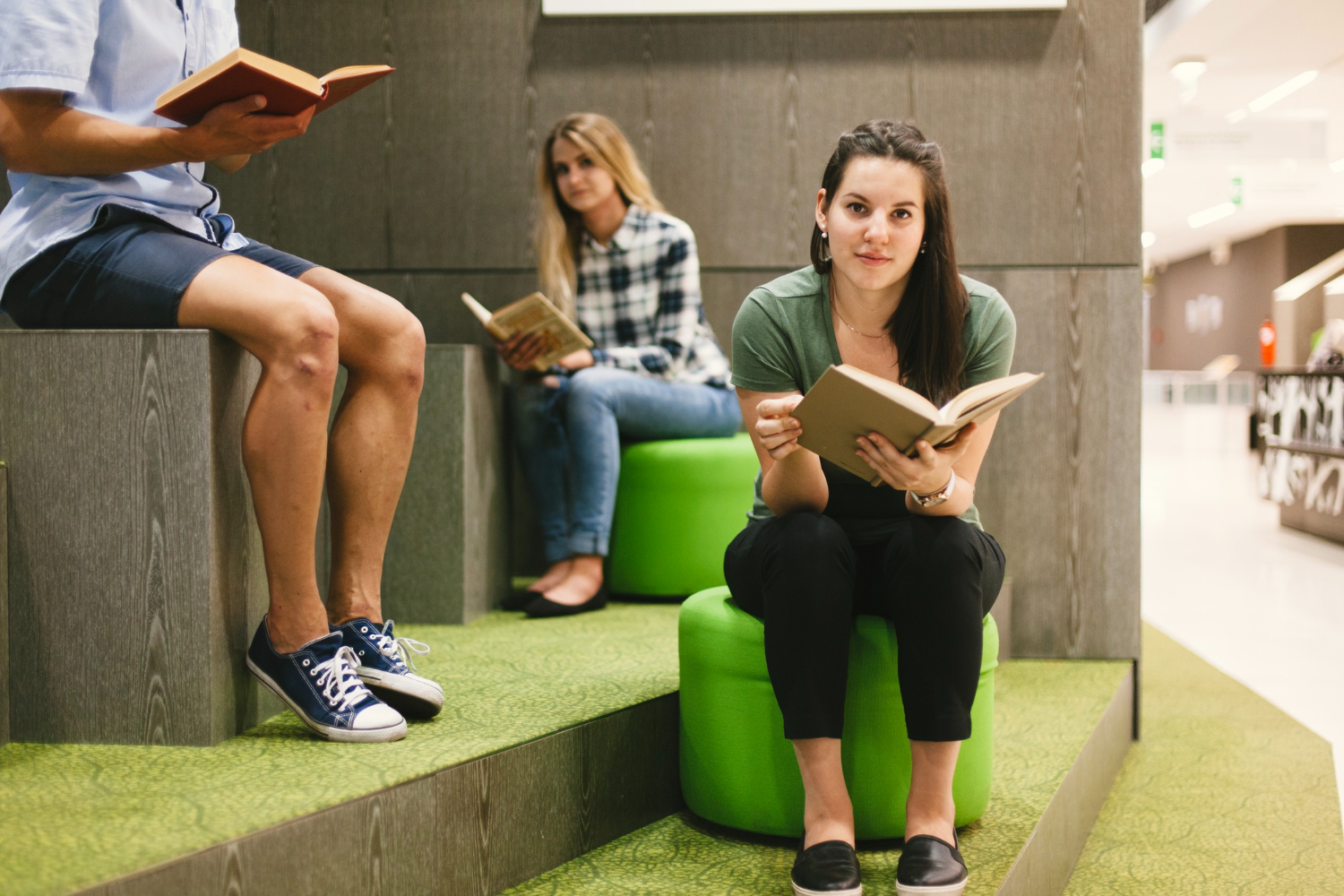 O que se estuda em Psicologia: três estudantes em uma biblioteca de faculdade, sentados em puffs e segurando um livro.