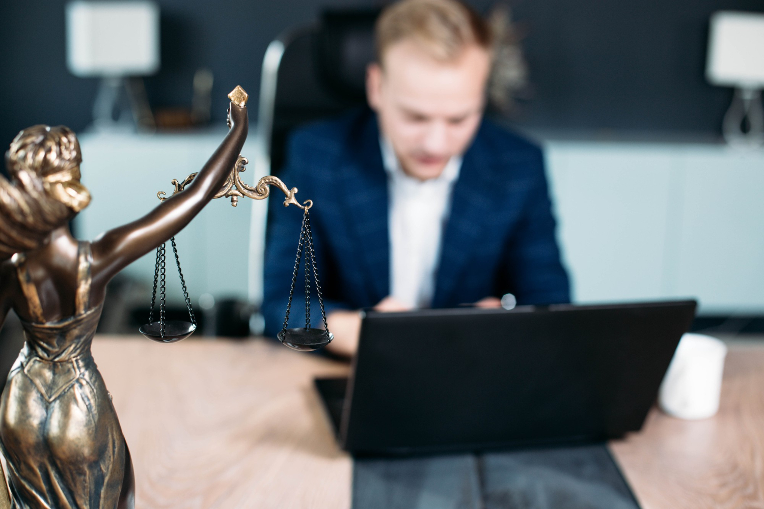 Advogado especialista em direito processual em seu escritório, utilizando um notebook para trabalhar. à sua frente, uma pequena estátua de Themis, Deusa da Justiça.