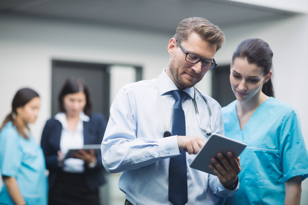 Gestor de experiência do cliente em serviço de saúde, em um consultório segurando um tablet, enquanto passa algumas orientações para uma funcionária