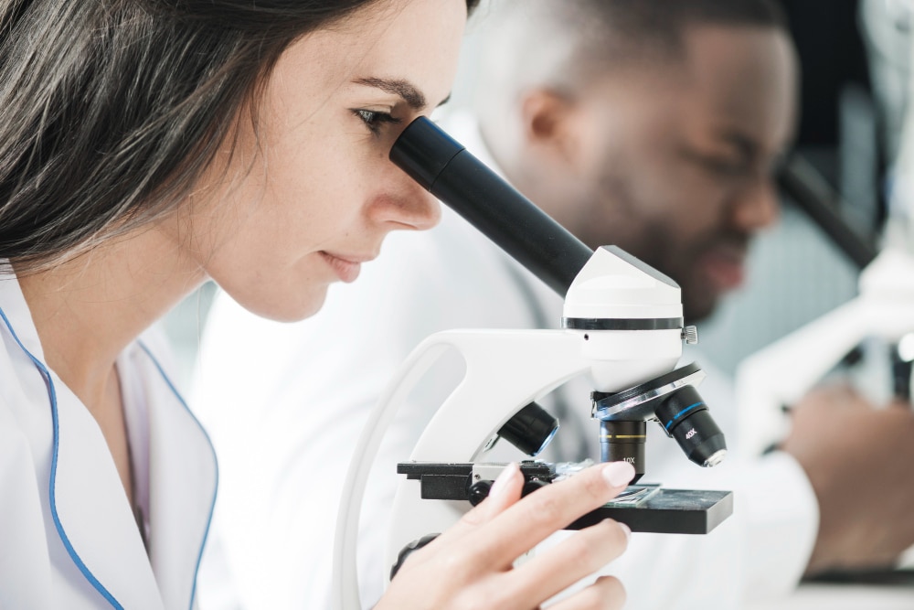 Jovem aluna de Medicina no laboratório da faculdade, utilizando o microscópio para analisar uma amostra de tecido durante uma aula de Histologia Humana