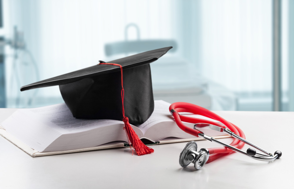 Juramento de medicina: capelo em cima de um livro aberto e um estetoscópio ao lado, representando a formação na área médica