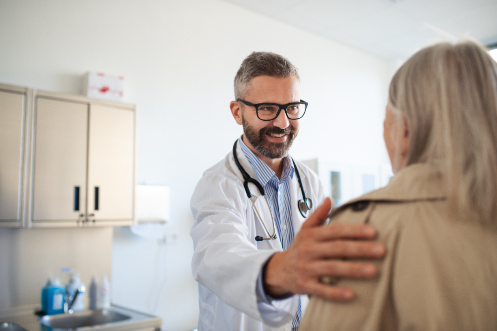 Médico sorridente com a mão no ombro de uma paciente, em sinal de cumprimento. Ele vai iniciar uma consulta dentro das diretrizes da Bioética Médica
