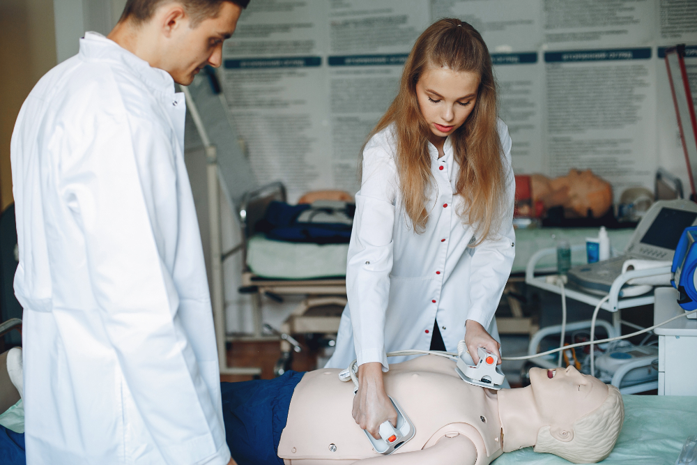 Aluna de Medicina em um laboratórios usando o desfibrilador em um manequim à sua frente, durante o ciclo clínico do curso.
