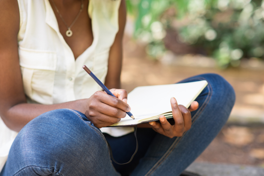 Jovem estudante sentada em uma área aberta, escrevendo em um caderno, treinando as regras de concordância verbal