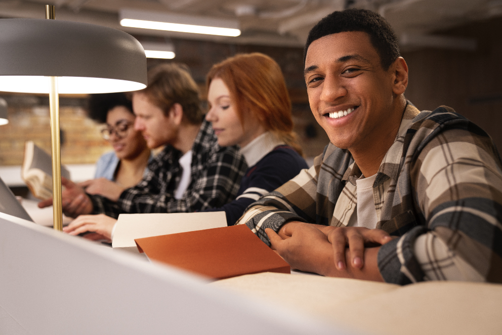 Jovem sorridente em uma sala de faculdade, ao lado de seus colegas, participando da Escola de Negócios