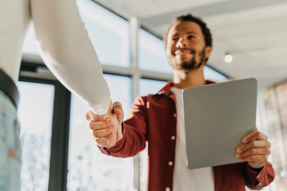 Jovem rapaz sorridente sendo cumprimentado por seu novo chefe, após ser contratado por possuir as habilidades do futuro necessárias para o cargo.