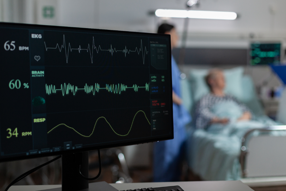 Monitor de um cardioversor monitorando os batimentos cardíacos de um paciente ao fundo.