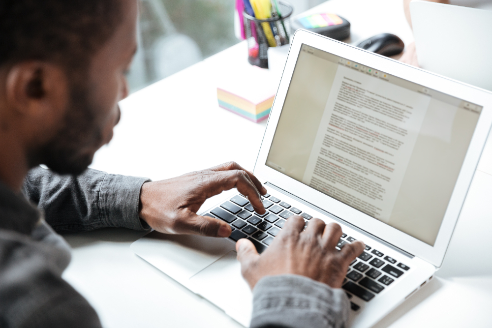 Jovem em busca de oportunidade no mercado utilizando um notebook para preencher seu currículo. Ele está incluindo o objetivo profissional para atrair os recrutadores.
