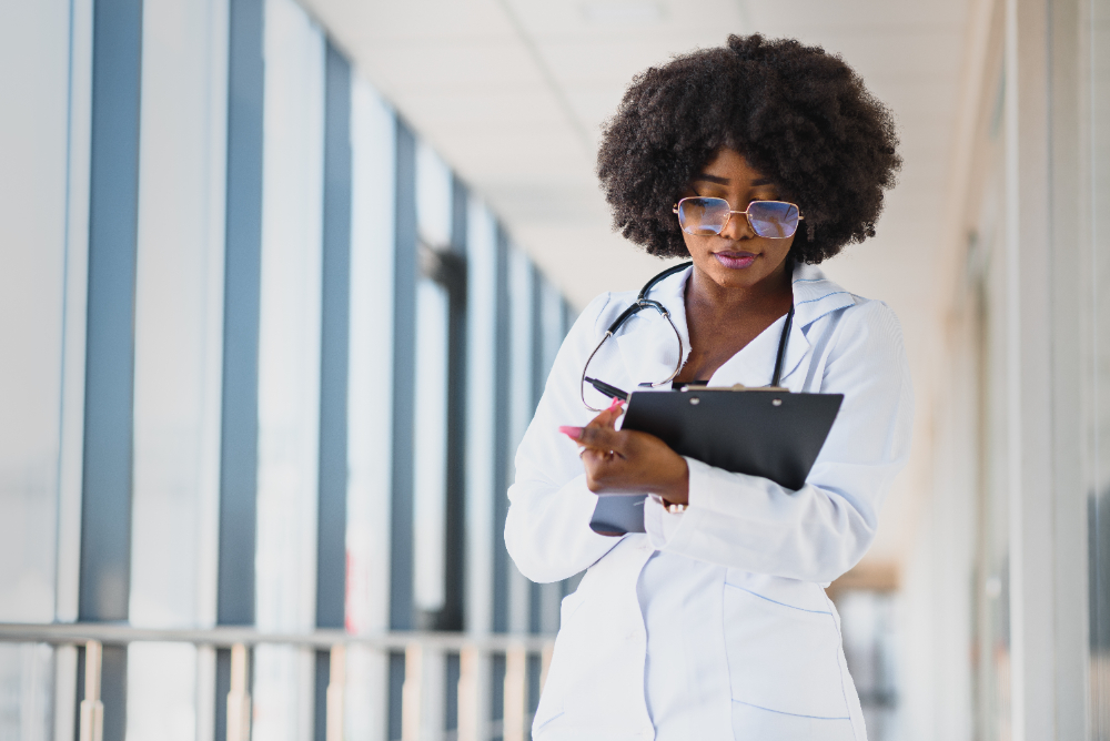 Jovem médica no corredor de um hospital, anotando informações e uma prancheta durante a residência médica.