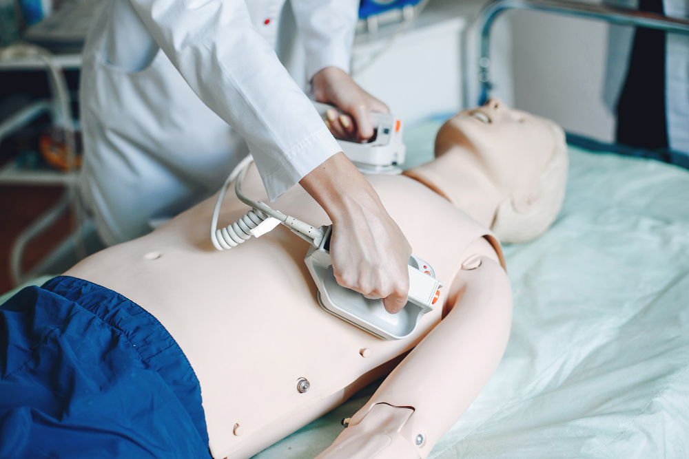 Estudante de medicina utilizando um desfibrilador em um manequim durante uma aula sobre os equipamentos hospitalares