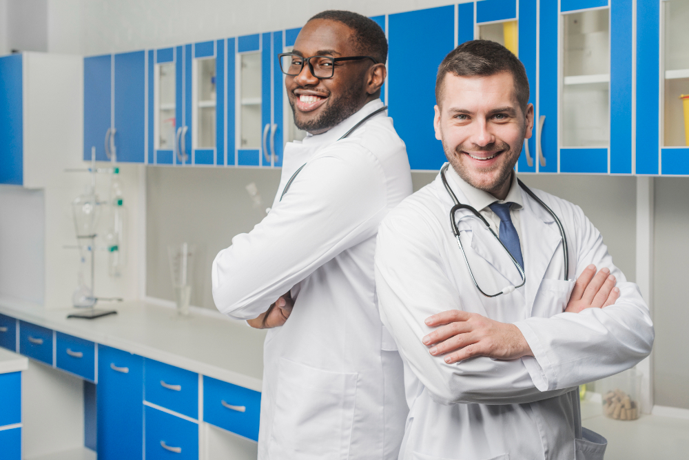 Medicina ou biomedicina? édico e biomédico lado a lado em um consultório, posando para a foto sorridentes e com os braços cruzados
