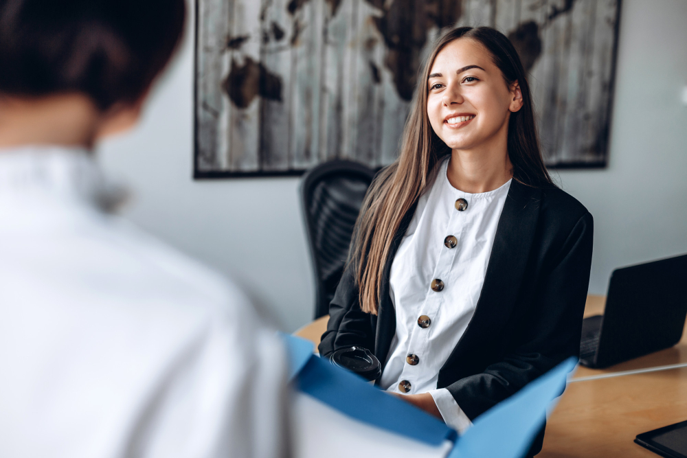 Jovem candidata sorridente durante uma entrevista de estágio em um ambiente corporativo, vestindo traje formal e demonstrando confiança enquanto conversa com o recrutador.