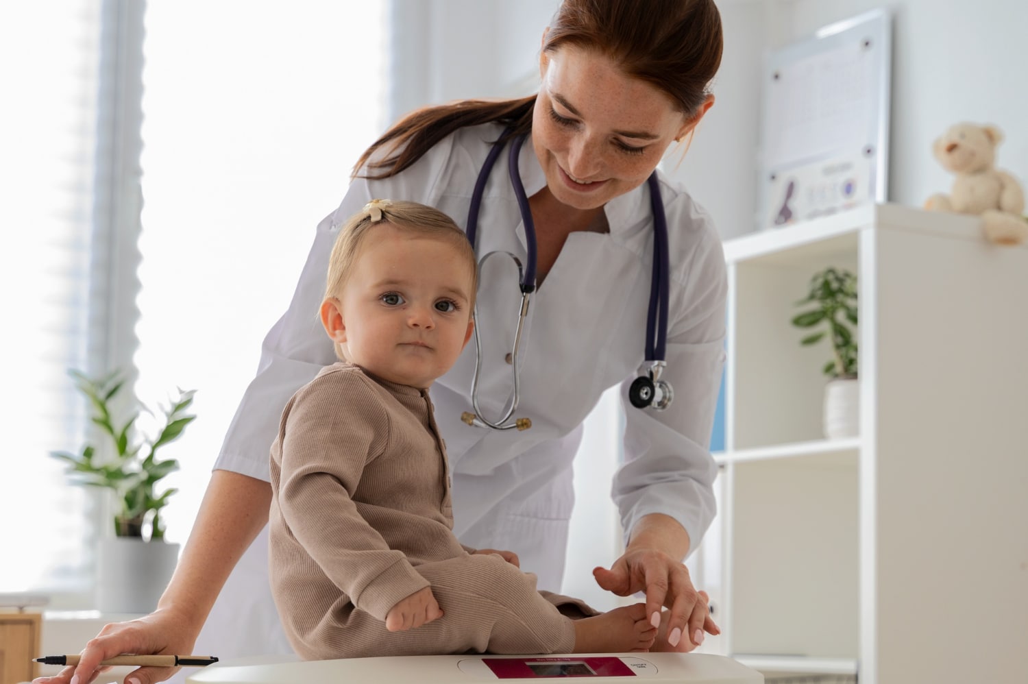 O que e pediatria: médica pediatra em seu consultório com um bebê sentado na maca durante o atendimento.