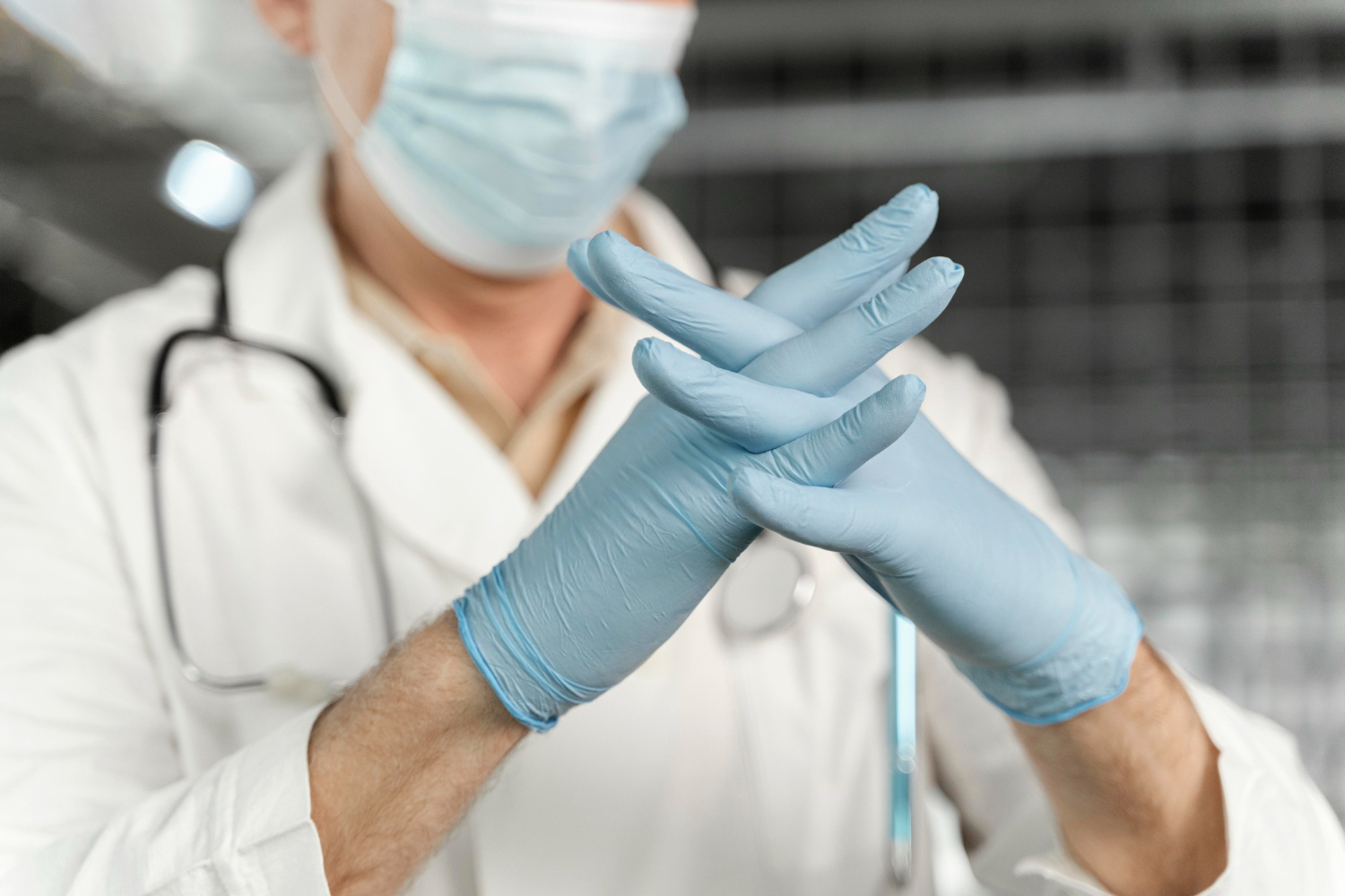 Médico com os dedos cruzados, utilizando suas luvas hospitalares antes de um procedimento.