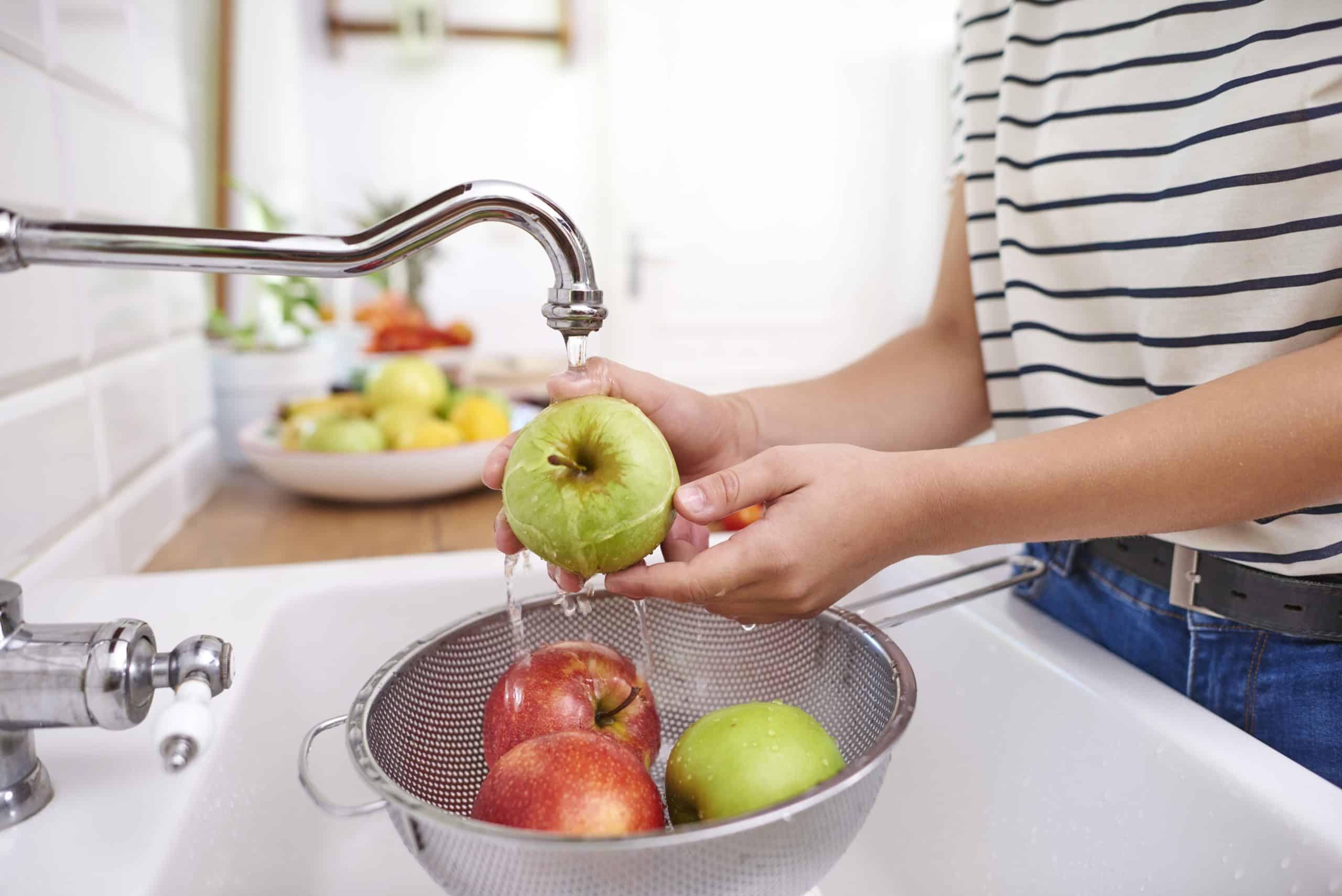 Pessoa lavando maçãs em água corrente para prevenir a contaminação alimentar.